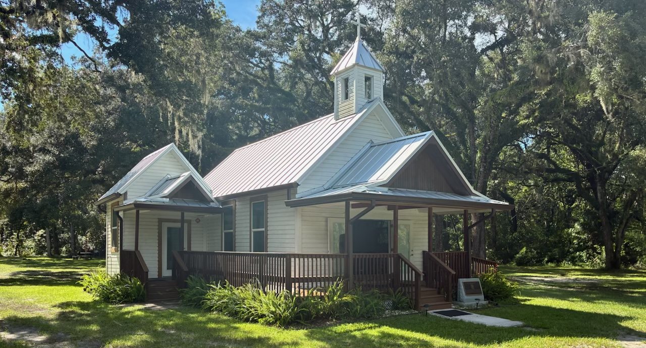 A small white clapboard chapel with a tin roof and bell tower, under live oaks hung with Spanish moss.