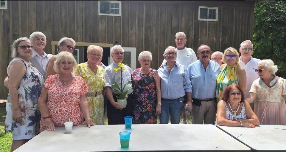 A group portrait of about sixteen people standing together outside the barn.